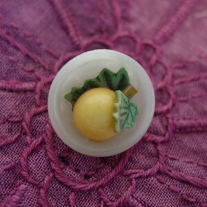 May include: A white ceramic dish with a green and yellow fruit design. The fruit is a stylized representation of a pear or apple.