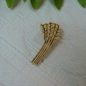 May include: A light beige wooden button shaped like a bundle of wheat stalks. The button features dark brown engraved lines that define the individual stalks and the textured grain pattern at the top of the wheat bundle, creating a detailed design.