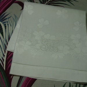May include: White linen hand towel with an embroidered floral pattern and the initials "S.H." in the center.