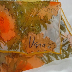 May include: A vintage silk scarf with a vibrant floral pattern in shades of orange, yellow, and olive green. The scarf features a repeating design with a signature "Vana" in black script. The edges are trimmed with a thin yellow border.
