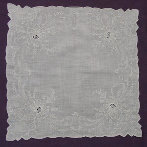 May include: A square white handkerchief featuring delicate white floral embroidery in each corner. The fabric has a scalloped edge with intricate needlework detailing, showcasing a symmetrical botanical pattern with leaves and vines.
