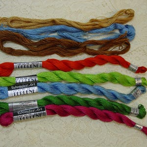 May include: A collection of eight spools of embroidery floss in various colors, including red, green, blue, and brown. Each spool is labeled "Wonder Art Perlene" and includes the art number and yardage.
