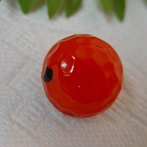 May include: A bright red, round, candy-like object with a black dot on one side. The object has a textured, dimpled surface.