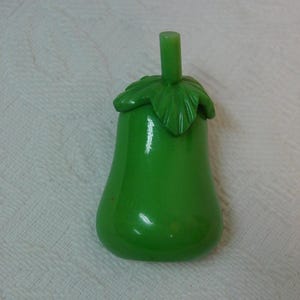 May include: A bright green pear-shaped object with a smooth, glossy finish. The top features a molded leaf design and a small, cylindrical stem extending upward from the center of the leaves, creating a stylized fruit-like appearance.