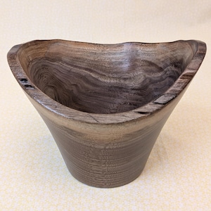 Puede incluir: Un cuenco de madera hecho a mano con un borde asimétrico único. El cuenco presenta un patrón de vetas de madera natural con tonos marrones y grises. La forma del cuenco es cónica, con una abertura ancha y una base robusta. Ideal para servir o decorar.