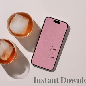 A smartphone with a pink screen displaying the text "Live in Love" and a faint "4 Tails Prints" watermark, positioned next to two round glass tumblers filled with amber-colored liquid and large square ice cubes.