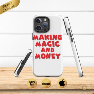 Pode incluir: Capa de telefone branca com o texto "MAKING MAGIC AND MONEY" em vermelho. A capa é mostrada com duas outras capas de telefone, uma preta e outra branca. A capa do telefone está em uma superfície de madeira.