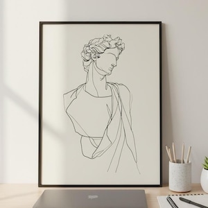 Può includere: Una stampa incorniciata in bianco e nero di un busto classico. L'opera d'arte è esposta su una scrivania in legno chiaro, insieme a un laptop, un blocco note con una penna, un portapenne e una piccola pianta grassa in vaso.