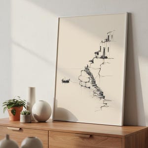 Puede incluir: Un boceto en blanco y negro enmarcado de una escena costera. La obra de arte representa una serie de escaleras que conducen a edificios en un acantilado. Un pequeño barco flota en el agua. La obra de arte se exhibe en un mueble de madera.