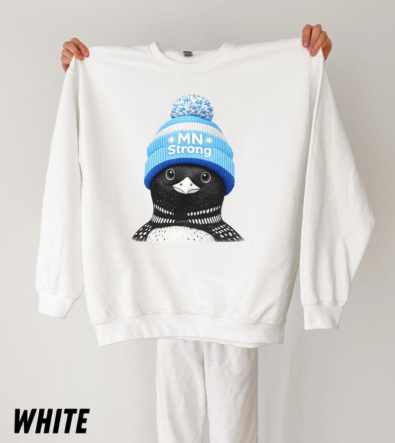 May include: White sweatshirt with a graphic of a loon wearing a blue and white knit hat with the text "MN Strong." The loon has black and white feathers and is centered on the front. The word "WHITE" is printed at the bottom.