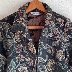 May include: A long-sleeve jacket featuring a dark green base with a woven floral tapestry pattern in shades of tan, brown, and muted pink. The jacket has a pointed collar, a button-front closure, and a white interior label reading robyne lune.