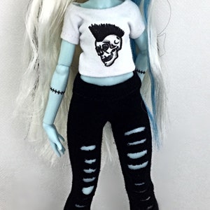May include: A blue-skinned doll with white and blue hair wearing a white t-shirt with a skull graphic and black ripped jeans. The doll is wearing black boots with silver studs.