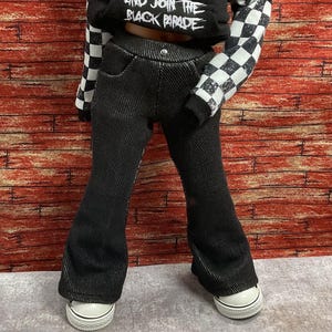 Könnte beinhalten: Schwarze Schlaghose kombiniert mit einem schwarzen Kapuzenpullover mit dem weißen Text AND JOIN THE BLACK PARADE und schwarz-weiß karierten Ärmeln. Das Outfit umfasst weiße Low-Top-Sneaker mit schwarzem Rand und strukturiertem Stoff.