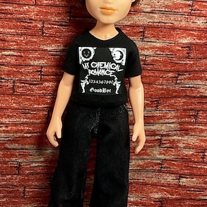 Könnte beinhalten: Puppe mit einem schwarzen T-Shirt mit dem Text "My Chemical Romance" und einer schwarzen Hose. Die Puppe hat braune Haare, blaue Augen und schwarze Schuhe mit braunen Akzenten. Der Hintergrund ist eine rote Backsteinmauer.