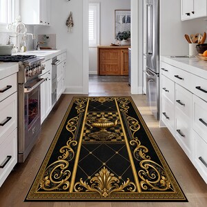 Può includere: Un tappeto da cucina rettangolare nero con un design dorato ornato. Il tappeto presenta un motivo centrale a urna dorata su uno sfondo a scacchi, incorniciato da volute dorate e bordi geometrici. Il tappeto è posto su un pavimento in legno.