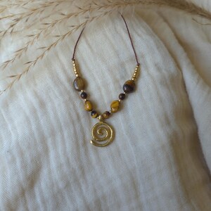 May include: A necklace featuring a gold-toned spiral pendant suspended from a thin brown cord. The design includes a series of polished tiger eye beads in shades of brown and gold, interspersed with small metallic gold-toned spacer beads.