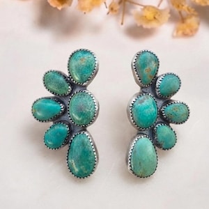 May include: A pair of stud earrings featuring multiple oval and teardrop-shaped turquoise stones set in silver. Each earring is arranged in a fan-like cluster pattern with five individual stones, showcasing natural blue-green colour variations.