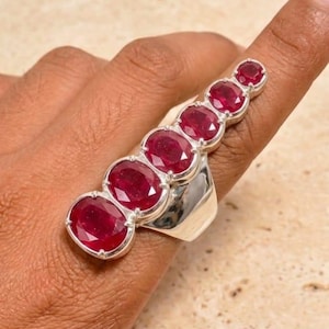 Peut inclure: Une bague en argent ornée d'une rangée verticale de six rubis rouge foncé taille ovale, dont la taille diminue du plus grand à la base au plus petit au sommet, sertis sur une bande en argent poli qui s'étend le long du doigt.
