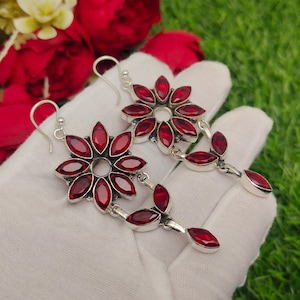Puede incluir: Pendientes colgantes plateados con diseño floral y pétalos de piedras preciosas rojas. Los pendientes tienen cierre de gancho y un acento colgante en forma de hoja. Las piedras preciosas son de color rojo intenso.