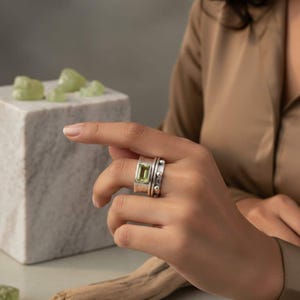 May include: A set of three ceramic mugs with a speckled, matte finish. The mugs are in shades of cream, light gray, and dark gray. Each mug has a simple, minimalist design and a rounded handle.