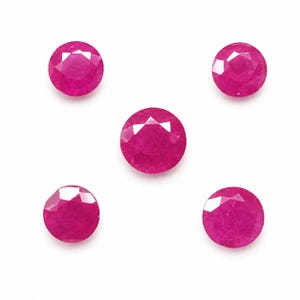 Könnte beinhalten: Fünf runde, facettierte, leuchtend pinkfarbene Rubine, die in einer Fünfeck-Formation angeordnet sind. Jeder Edelstein weist einen Brillantschliff mit mehreren dreieckigen Facetten auf, die das Licht reflektieren und eine tief gesättigte magentafarbene Tönung zeigen.