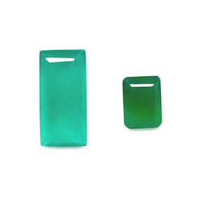 Könnte beinhalten: Zwei Smaragd-Edelsteine in Grüntönen. Der größere Stein ist ein leuchtendes, helles Grün, während der kleinere ein tieferes, dunkleres Grün aufweist. Beide haben eine rechteckige Form mit flacher Ober- und Unterseite.