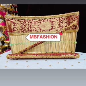 Peut inclure: Un panier rectangulaire en bambou avec une bordure décorative à motifs rouges et dorés. Le panier a une tige décorative rouge et or assortie. Le texte "MBFASHION" est affiché sur un panneau blanc en forme de flèche.