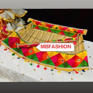 Peut inclure: Un panier rectangulaire décoratif avec une base en bambou et une bordure brodée colorée. La bordure présente des motifs géométriques roses, oranges, verts et jaunes, avec de petits miroirs et des perles suspendues. Le texte "MBFASHION" est affiché sur le côté.