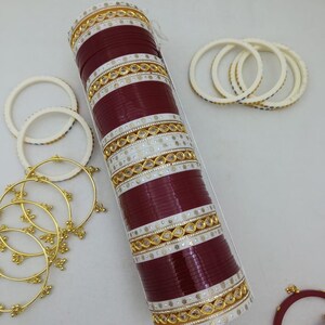 Könnte beinhalten: Eine Sammlung roter und weißer Armreifen mit goldenen Akzenten. Der Hauptstapel der Armreifen befindet sich in einer transparenten Hülle. Zusätzliche weiße und goldene Armreifen sind um den Hauptstapel herum verstreut.
