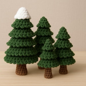 Puede incluir: Un conjunto de cuatro árboles de Navidad hechos a mano con ganchillo. Los árboles, de varios tamaños, tienen follaje verde y troncos marrones. Uno de ellos tiene una cima blanca, como de nieve. Están colocados sobre una superficie clara.