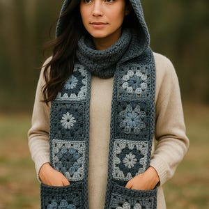 May include: A hooded scarf in shades of blue and gray, featuring a granny square design. The scarf has pockets and a matching cowl neck. The woman in the image is wearing a beige sweater and the scarf is draped over her shoulders.