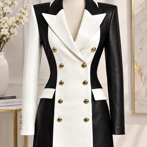 May include: A double-breasted blazer dress featuring a color-blocked design with a white center panel and black side panels. It has a notched lapel, long sleeves, two flap pockets, and ten gold-toned buttons arranged in two vertical rows.