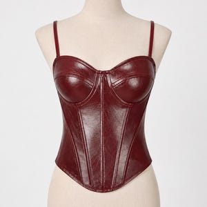 May include: A burgundy-colored bustier top with thin shoulder straps. The bodice features a structured design with vertical seams and a sweetheart neckline. The top is displayed on a mannequin.