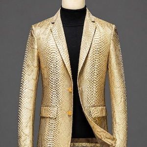 May include: A gold snakeskin-patterned blazer on a mannequin. The blazer features two gold buttons, two front pockets, and a notched lapel. A black turtleneck is worn beneath the blazer, creating a striking contrast.