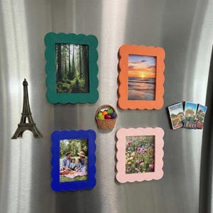 Puede incluir: Un conjunto de imanes decorativos para nevera. Los imanes incluyen cuatro marcos de fotos con bordes festoneados en verde, naranja, azul y rosa, cada uno con una imagen diferente. También se incluye una Torre Eiffel en miniatura y una cesta de frutas.