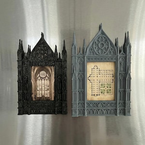 Könnte beinhalten: Zwei Bilderrahmen im gotischen Stil. Einer ist schwarz und enthält ein Bild eines Buntglasfensters. Der andere ist grau und zeigt einen Kirchengrundriss. Beide Rahmen weisen komplizierte architektonische Details auf, die an Miniatur-Kathedralenfenster erinnern.