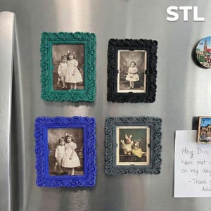 May include: Four framed vintage photographs with ornate frames in teal, black, blue, and gray. The photos depict children and a pair of stuffed animals. The frames are attached to a stainless steel surface.