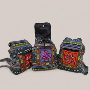 Könnte beinhalten: Drei farbenfrohe Rucksäcke mit Muster, Kordelzug und Klappe. Jeder Rucksack hat ein zentrales gesticktes Design mit einem Sternmuster in Rosa-, Orange- und Lilatönen. Die Taschen haben eine Vielzahl von Farben, darunter Blau, Grün und Gelb.