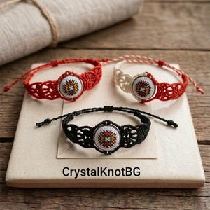 May include: Three macrame bracelets in red, cream, and black, each featuring a central embroidered medallion with a colorful floral design. The bracelets are displayed on a light-colored square tile, with the text "CrystalKnotBG" visible.