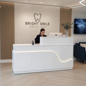 May include: A white, glossy reception desk with a curved, illuminated front panel. Behind the desk, a wall features vertical wood slats and a silver sign reading BRIGHT SMILE DENTAL CARE with a tooth icon. A computer monitor sits on the desk.