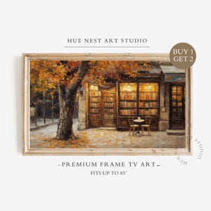 May include: A framed digital art print for a television screen featuring an oil painting of a bookstore exterior with a large tree displaying orange autumn leaves, a small bistro table with two chairs, and shelves filled with books inside.