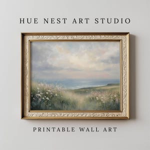 Puede incluir: Pintura de paisaje enmarcada con una escena costera y flores silvestres en primer plano. La obra de arte tiene un marco dorado y ornamentado. El texto "HUE NEST ART STUDIO" y "PRINTABLE WALL ART" se muestran arriba y abajo.