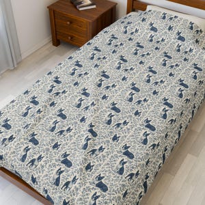May include: A twin-sized bed covered with a patterned comforter. The comforter features a repeating design of blue Boston Terrier dogs and floral elements on a cream background. The bed is made of wood and has a wooden nightstand next to it.