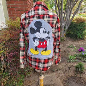 May include: Red and black plaid flannel shirt with a gray Mickey Mouse patch on the back.