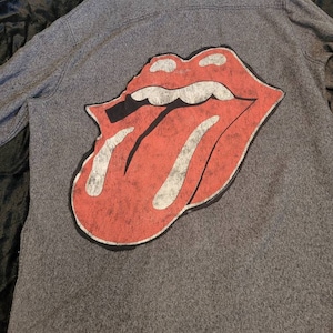 May include: A gray long-sleeved shirt with a red and white tongue graphic on the back. The tongue graphic is a classic rock and roll symbol.