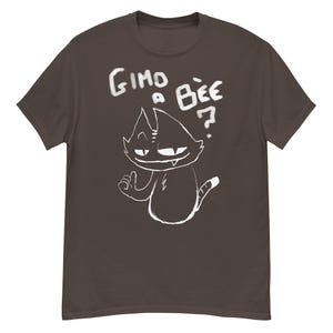 May include: A dark brown t-shirt featuring a white cartoon cat illustration with the text "Gimo a Bee?" The cat has a smug expression and is giving a thumbs up. The design is hand-drawn in a sketchy style.
