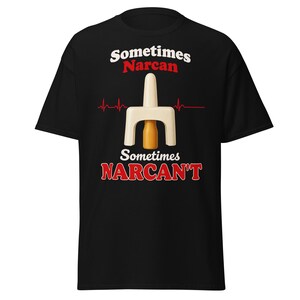 May include: A black short-sleeve t-shirt featuring a graphic of a nasal spray device and a heartbeat line. The text reads Sometimes Narcan in white and red, and Sometimes NARCAN'T in white and red, centered on the chest of the garment.