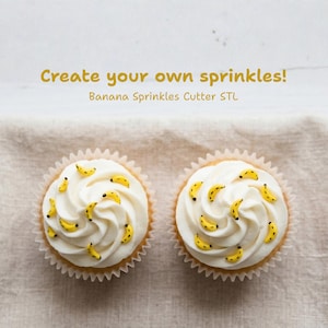 May include: Two cupcakes with white icing and yellow banana sprinkles. The cupcakes are in white paper cases and sit on a beige surface. Text in the image reads: "Create your own sprinkles! Banana Sprinkles Cutter STL."