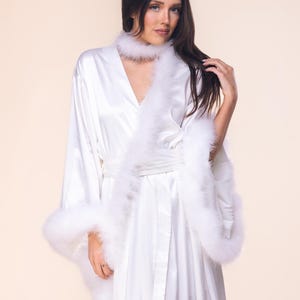 May include: A white satin robe with feather trim on the cuffs and lapels. The robe has a matching feather collar and a tie belt. The long-sleeved robe is a luxurious garment.