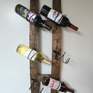 May include: A rustic wooden wine rack with four bottles of wine. The rack is made from reclaimed wood and features black metal holders. The wine bottles are various colors, including green, white, and red, and are held at an angle.